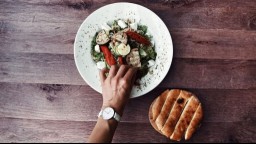 close-up of hand with watch on wrist reaching for a plate of vegetables