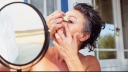 person with short black hair using eye drops in front of a round mirror