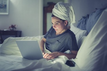 woman in bed at night working with hair in towel