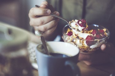 person eating yogurt, granola, berries for breakfast