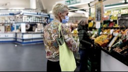 person with floral print blouse, short bleached hair, and face mask shopping for food in a supermarket