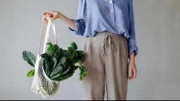 A close up of a woman holding a netted shopping bag full of dark collard greens or cabbage