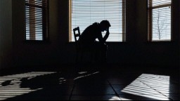 A man holds his head in his hands as he sits on a bed