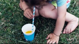 Close up of a child drinking orange juice from a disposable cup with a straw on grass outside