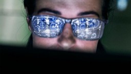 A man wears blue-tinted glasses that reflect brain scans