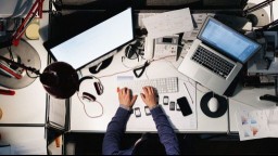 An overhead view of a man working at a desk with two active screens