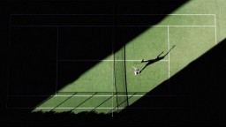 An aerial shot of tennis match from above with the player's shadow reflecting onto the court