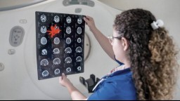 female researcher with long curly hair holding up brain scan