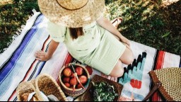 A pregnant woman sits on a blanket next to baskets of apples, nuts, and greens