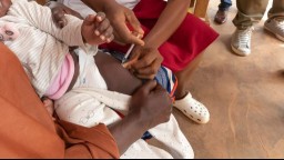 close-up of Black parent holding their small child as they receive the malaria vaccine