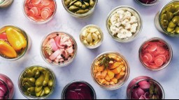 Clear glass bowls full of colorful, fermented, pickled vegetables against a white marble background.