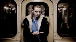 A woman standing in a subway car listens to music on her iPhone