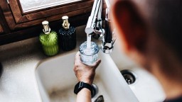 A man at a kitchen sink pours a glass of water