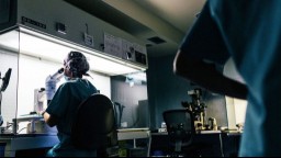 Scientist in lab examining cancer cells through microscope