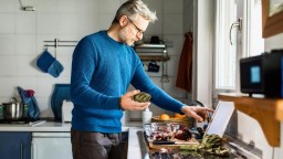 A man holds an artichoke in his kitchen while reading a recipe