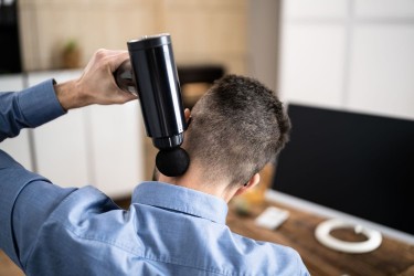 man using massage gun on neck