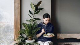 A woman eating a plate of food depicting a health meal plan while sitting next to a potted plant