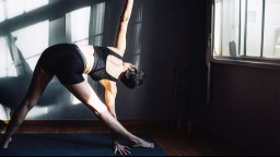 A woman stretches her back while doing yoga exercises near a window