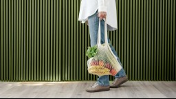 A close-up of a person carrying vegetables in a knit, reusable grocery bag.