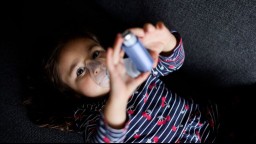 A child using an asthma inhaler lays on the floor