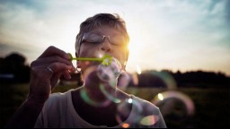 An older woman standing outside blows bubbles